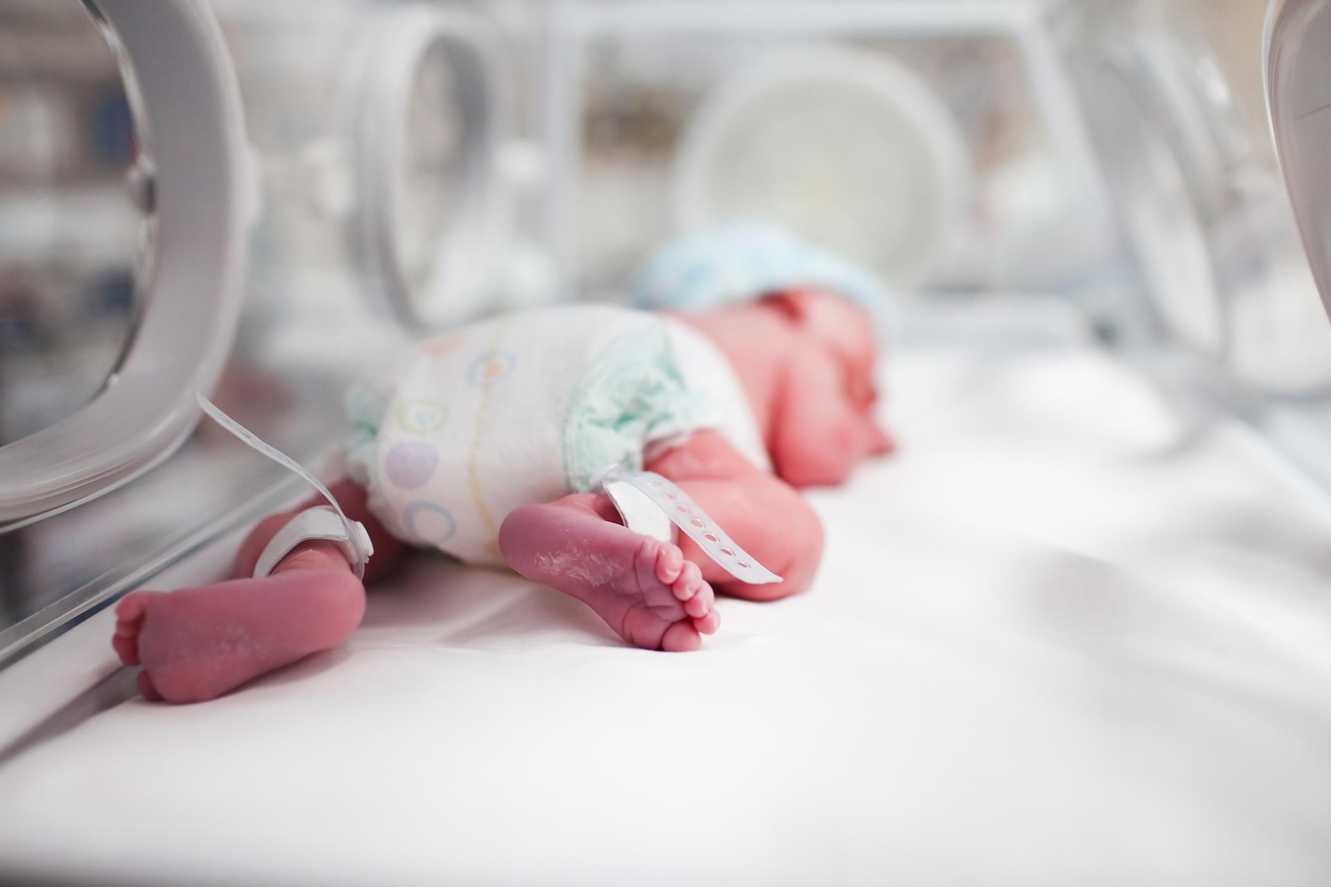 Newborn baby boy covered in vertix inside incubator